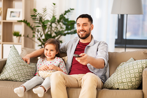family, fatherhood and people concept - happy father and daughter with popcorn watching tv at home