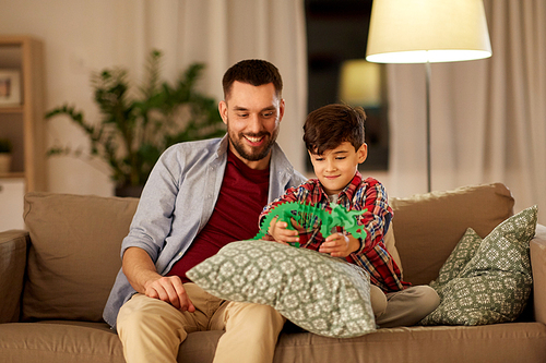 family, fatherhood and people concept - happy father and son playing with toy dinosaur at home in evening