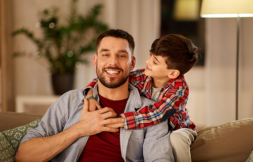 family, childhood, fatherhood, leisure and people concept - portrait of happy smiling father and little son hugging at home in evening