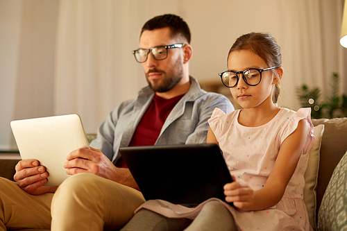 family, fatherhood and technology concept - father and daughter in glasses with tablet pc computers at home in evening
