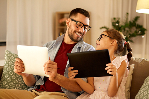 family, fatherhood and technology concept - happy father and daughter in glasses with tablet pc computers at home in evening