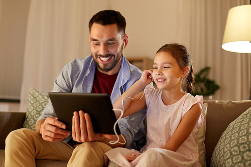 family, fatherhood and technology concept - happy father and little daughter with tablet pc computer and earphones listening to music at home in evening