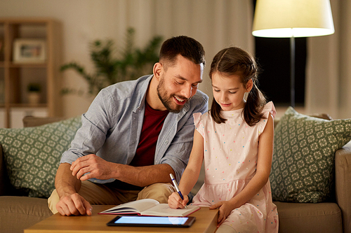 education and family concept - happy father and daughter with book and tablet computer doing homework together at home in evening