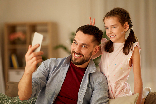 people, family and technology concept - happy father and little daughter taking selfie by smartphone at home