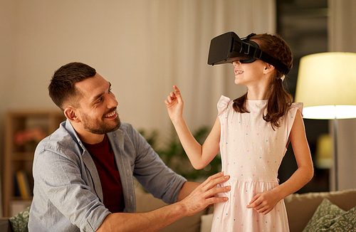 family, virtual reality and entertainment concept - happy father and little daughter with vr glasses playing video game at home in evening