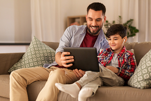 family, fatherhood and technology concept - happy father and little son with tablet pc computer and earphones listening to music at home