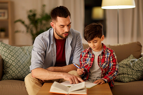 education, family and homework concept - father and son with book writing to notebook at home in evening