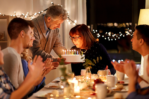 celebration and family concept - happy grandmother blowing candles on birthday cake at dinner party at home