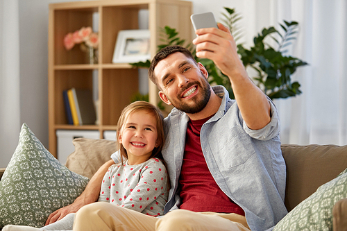 people, family and technology concept - happy father and little daughter taking selfie by smartphone sitting on sofa at home