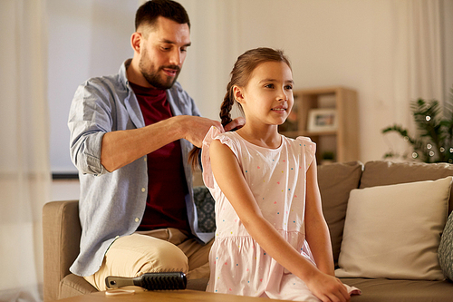 family and people concept - happy father braiding daughter hair at home in evening