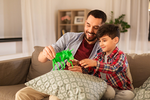 family, fatherhood and people concept - happy father and son playing with toy dinosaur at home