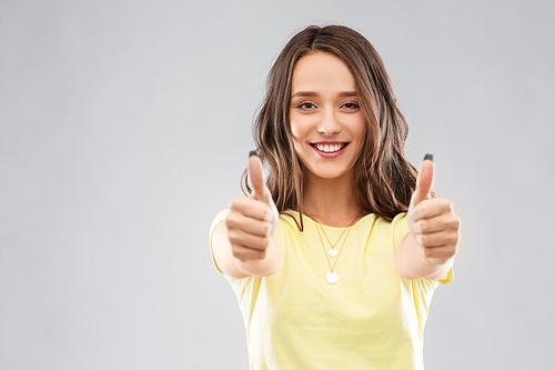 gesture and people concept - smiling young woman or teenage girl in blank yellow t-shirt showing thumbs up over grey background