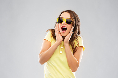 summer, accessory and people concept - amazed young woman or teenage girl in yellow t-shirt and sunglasses over grey background