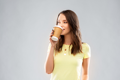 takeaway and people concept - young woman or teenage girl in yellow t-shirt drinking coffee over grey background