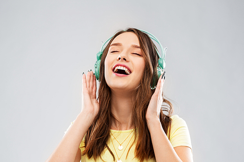 music, technology and people concept - happy young woman or teenage girl with headphones over grey background