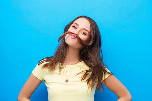hairstyle and people concept - young woman or teenage girl making mustache with strand of hair over bright blue background