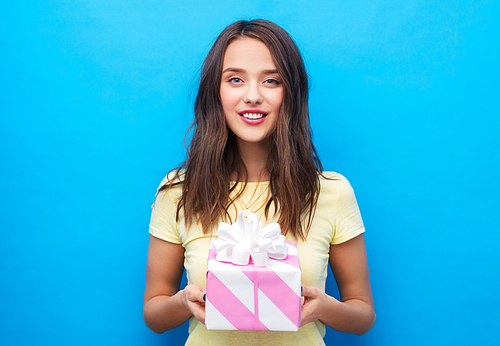 birthday and people concept - smiling young woman or teenage girl in yellow t-shirt with gift box over bright blue background