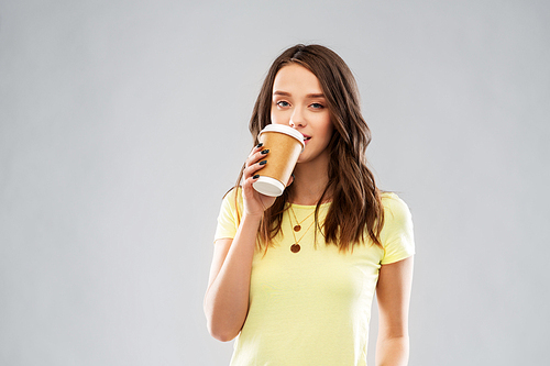 takeaway and people concept - young woman or teenage girl in yellow t-shirt drinking coffee over grey background