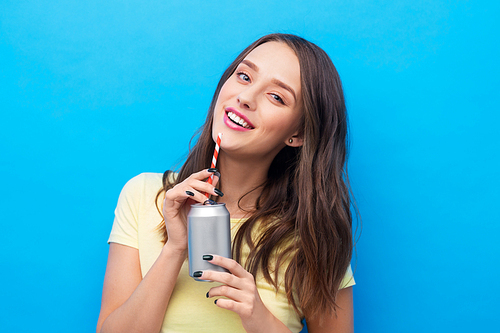 people concept - smiling young woman or teenage girl in yellow t-shirt drinking soda from can through paper straw over bright blue background