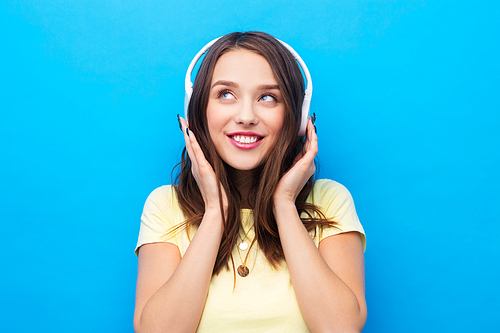 music, technology and people concept - happy young woman or teenage girl with headphones over bright blue background