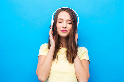 music, technology and people concept - happy young woman or teenage girl with headphones over bright blue background