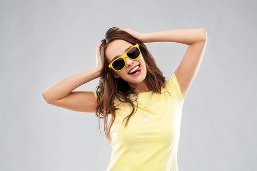 summer, accessory and people concept - smiling young woman or teenage girl in yellow t-shirt and sunglasses holding to her head over grey background