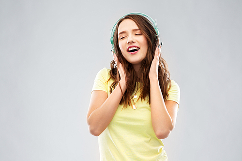 music, technology and people concept - happy young woman or teenage girl with headphones over grey background