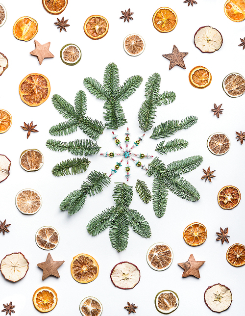 Snowflake made with fir or pine branches and dried fruits and spices on white desk background. Creative layout for Christmas or winter holidays greeting cards, top view