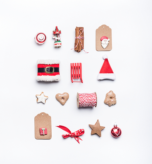 Creative Christmas layout made of craft paper tags, cookies, red Christmas winter decoration: Santa hat, sleigh, cinnamon sticks on white desk background, top view, flat lay. Holiday pattern
