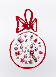 Christmas decoration objects laid out in  shape of Christmas bauble with ribbon on white background, top view