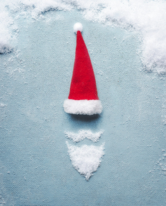 Santa Claus symbol made with snow and Santa hat on blue background. Christmas card . Creative minimal holiday concept
