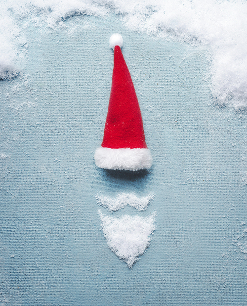 Santa Claus symbol made with snow and Santa hat on blue background. Christmas card . Creative minimal holiday concept