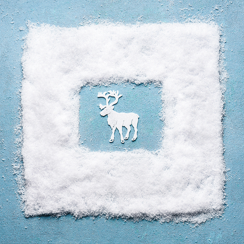 Creative Christmas concept with white deer in snow frame on light blue background, top view. Festive greeting card. Winter holiday concept