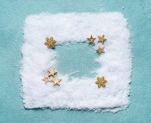 Christmas background frame made with snow on blue background with golden stars decoration, top view, flat lay. Winter composition and holiday concept