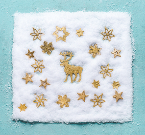 Christmas reindeer in snow with golden snowflakes on light blue background, top view. Flat lay. Winter composition and holiday concept