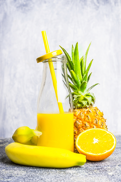 yellow smoothie bottle with straw and ingredients on light wooden background, side view. healthy lifestyle and detox or   food concept