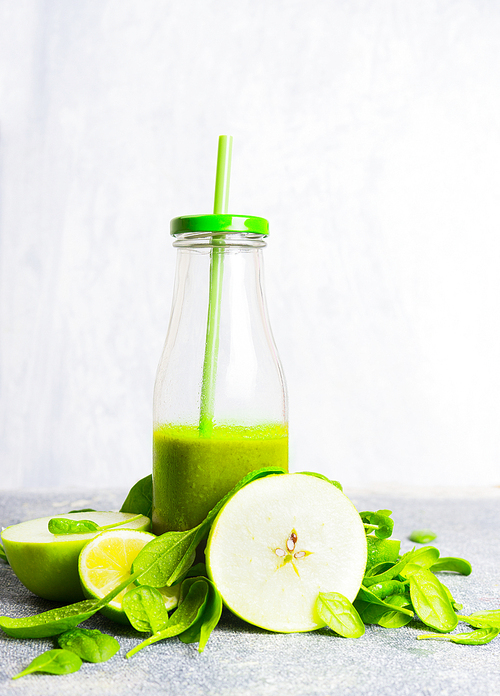Green smoothie bottle with straw and green ingredients on light wooden background, side view. Healthy lifestyle and detox or diet  food concept