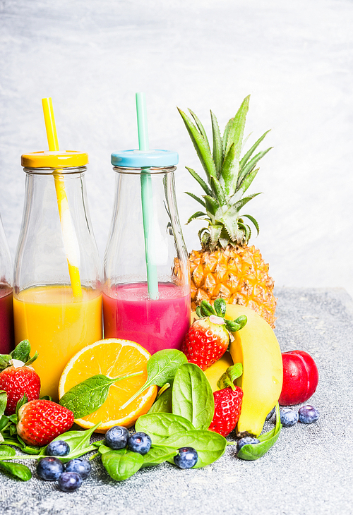 Red and yellow smoothies drinks in bottles with fruits ingredients on light background. Healthy lifestyle, Detox or diet food concept.