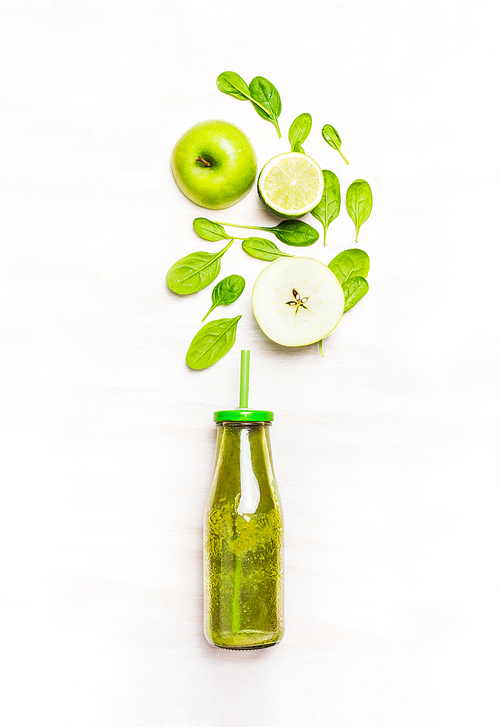 Green smoothie drink in bottle with straw  and  ingredients ( spinach,apple, lime )  on white wooden background, top view