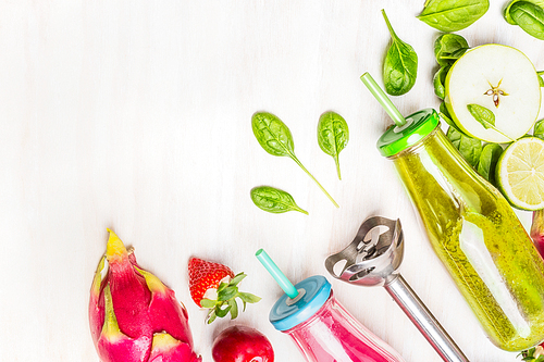 Healthy Food with pink and green smoothies in bottles with straws and ingredients: apple, lime, spinach, strawberries, plums, exotic fruit on white wooden background, top view, border