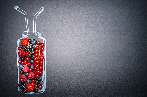 Painted bottle with fresh various berries for smoothie or juice making on dark chalkboard background, place for text