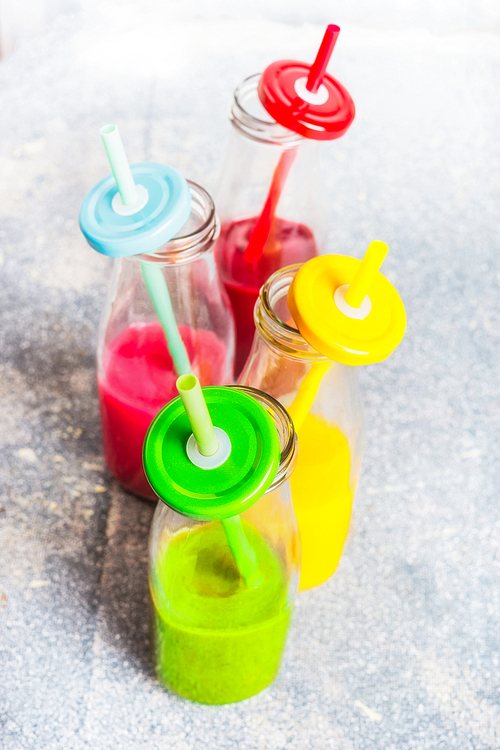 variety of colorful smoothies in bottles  with  straws: green,yellow,red.