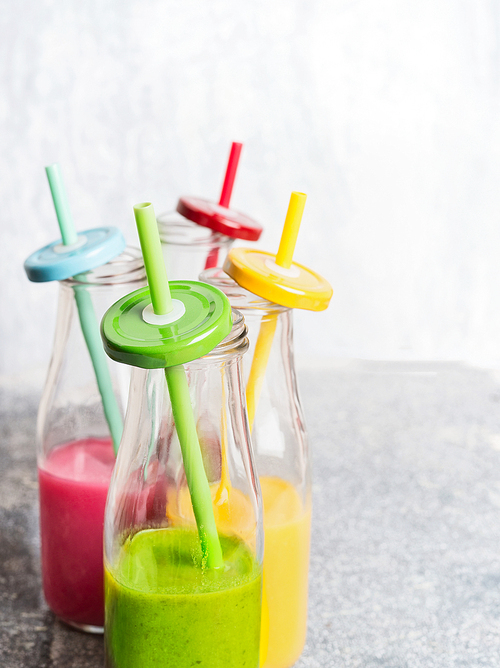 various of colorful smoothie in bottles  with  straws: green,yellow,red, front view, close up