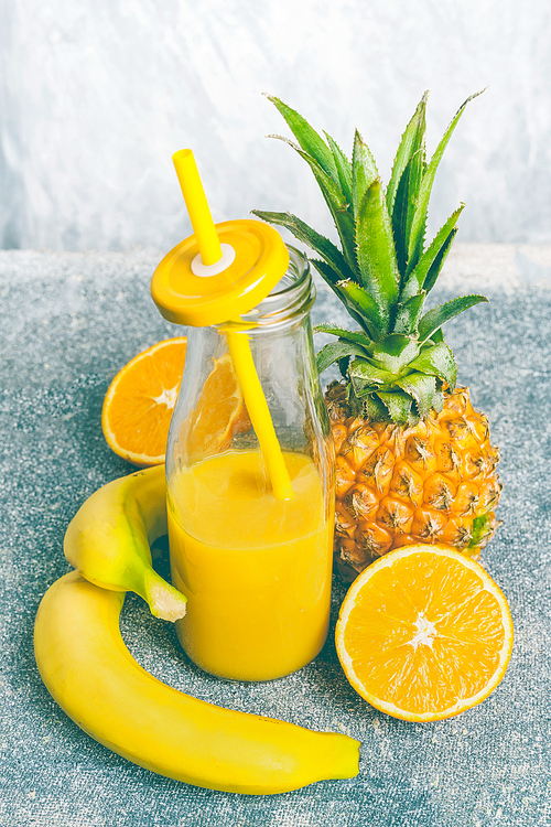 yellow fruits smoothie in bottle with  straw and fresh ingredients: banana, orange and pineapple, front view, copy space