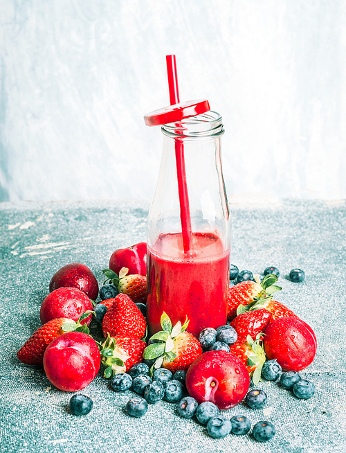 red smoothie  in bottle with berries and fruits ingredients on light background, front view.  healthy,  or detox beverage concept