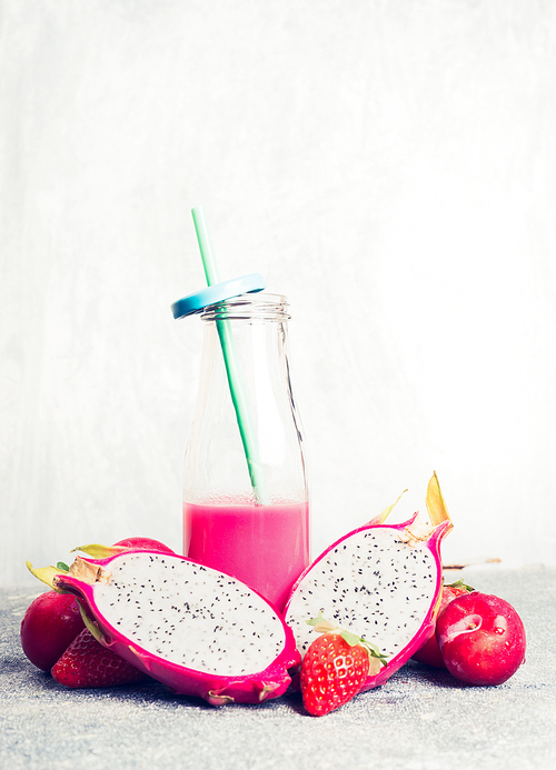 pink smoothie  in bottle with tropical fruits ingredients on light background, front view.  healthy,  or detox beverage concept