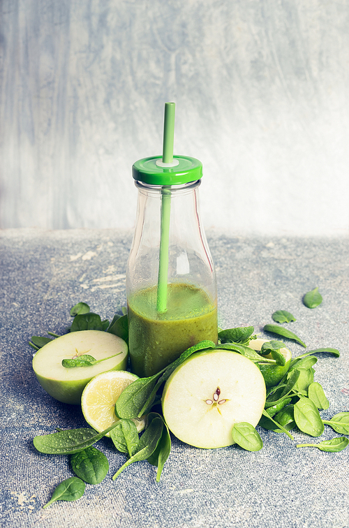 Green smoothie in bottle and ingredients: apple and spinach, on rustic background, front view, retro toned.  Healthy, diet or detox beverage concept