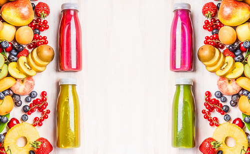 Red,pink,green and yellow smoothies and juices beverages in bottles with various fresh organic fruits and berries ingredients on white wooden background, top view. Healthy food concept