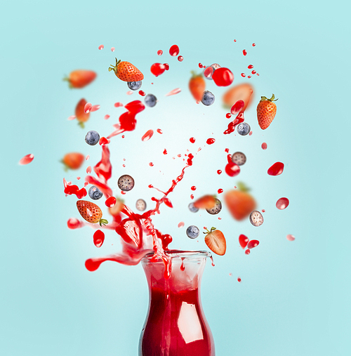 Red juice or smoothie drink is poured out of glass bottle with splash and berries ingredients on turquoise background, front view. Healthy summer beverage concept