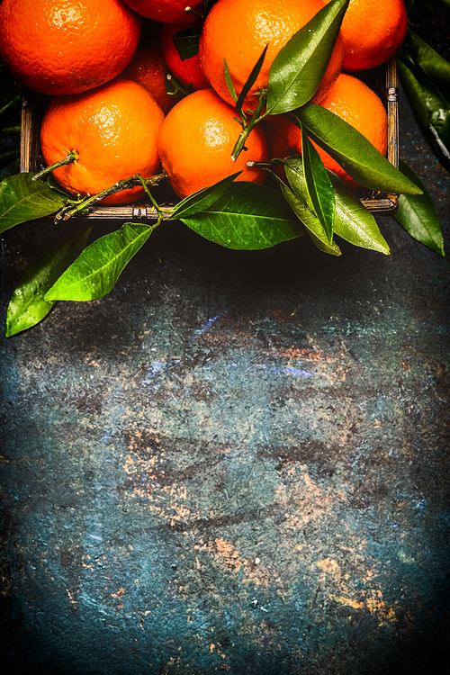 Fresh tangerines with green leaves on dark rustic background, top view, border
